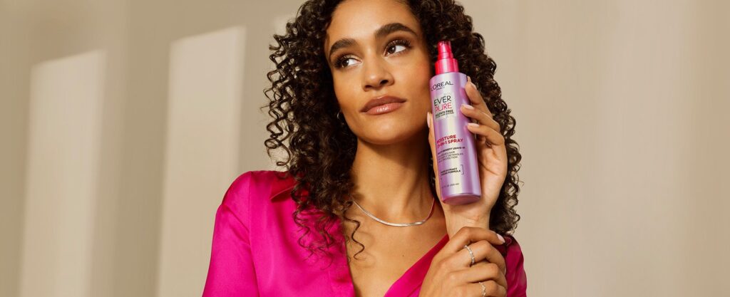 Woman holding heat protectant spray before using hair straightener โ Step 6 in haircare routine