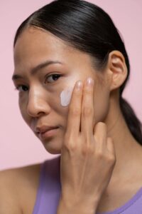 Woman with dark skin applying sunscreen on her face.